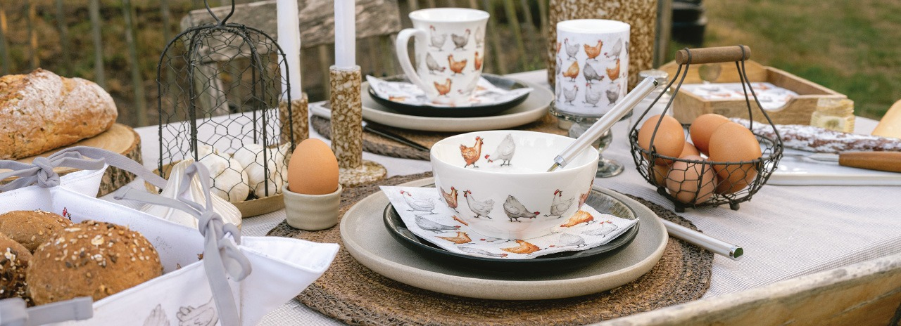 Stilvoll gedeckter Tisch mit 'Cackling chickens' Geschirr, Schüsseln mit Hühner-Print und Eiern.