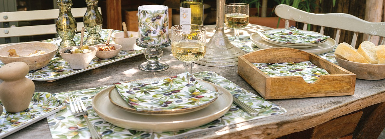 Stilvoll im mediterranen Stil gedeckter Esstisch mit 'Culinary olives' Geschirr, Servietten und Häppchen