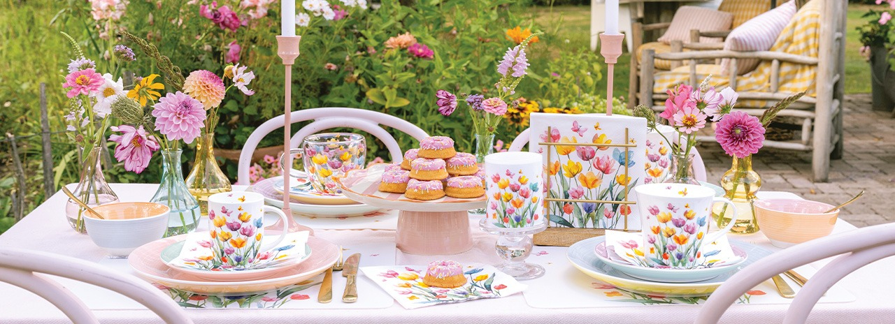 wunderschön gedeckter Gartentisch mit 'Fantasy flowers' Geschirr, bunten Blumen und süßen Leckereien.