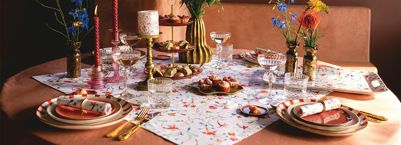 Warm-toned dining table tastefully set with 'Florence' tableware, red candles, and treats.