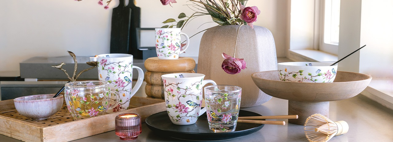 Présentation élégante de mugs, verres et bols 'Lively blossom tree' ornés d'un motif de fleurs et d'oiseaux.