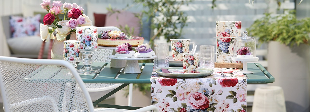 Stilvoll gedeckter Gartentisch mit 'Rosemary' Geschirr, Rosen-Textilien und süßen Leckereien.