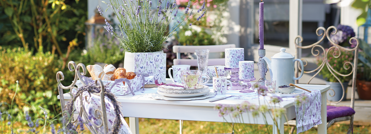 Gartentisch gedeckt mit Geschirr, Textilien und Blumentopf der Serie 'Butterfly lavender'.