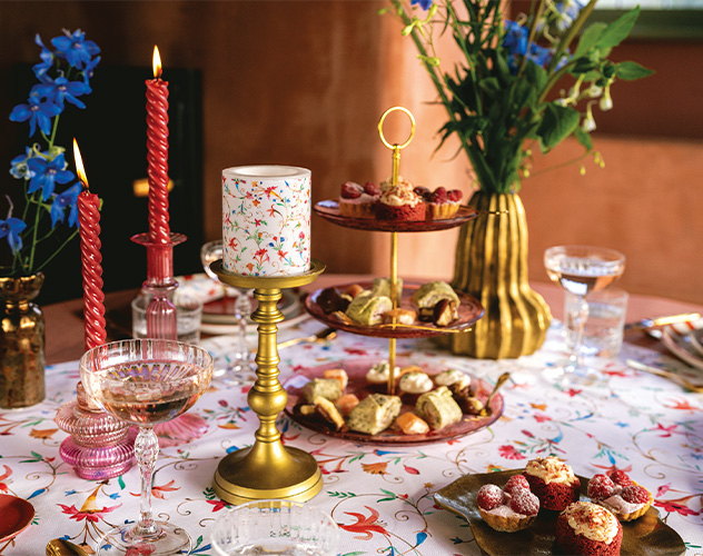 Gedekte tafel met 'Florence' kaars op een gouden kandelaar, etagère met lekkernijen en rode dinerkaarsen.