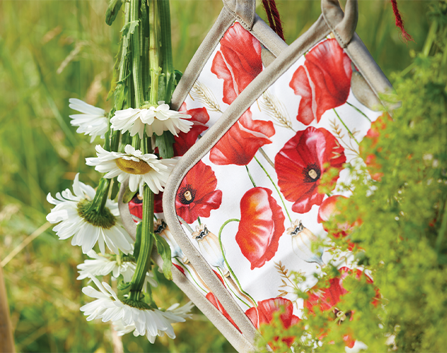 Zwei Topflappen mit rotem 'Poppy all over' Mohnblumen-Print, aufgehängt im Grünen.
