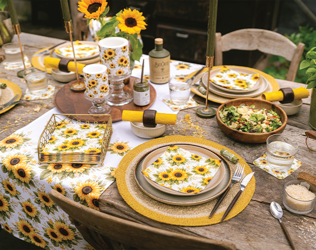 Gezellige eettafel gedekt met 'Sunflower pattern' servetten, kaarsen en zonnebloemen.