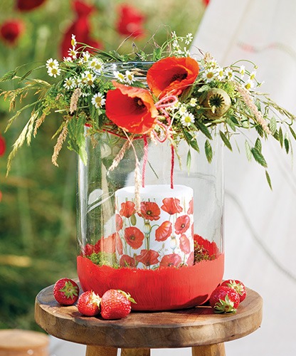 Large glass lantern featuring a 'Poppy all over' candle topped with wildflowers.